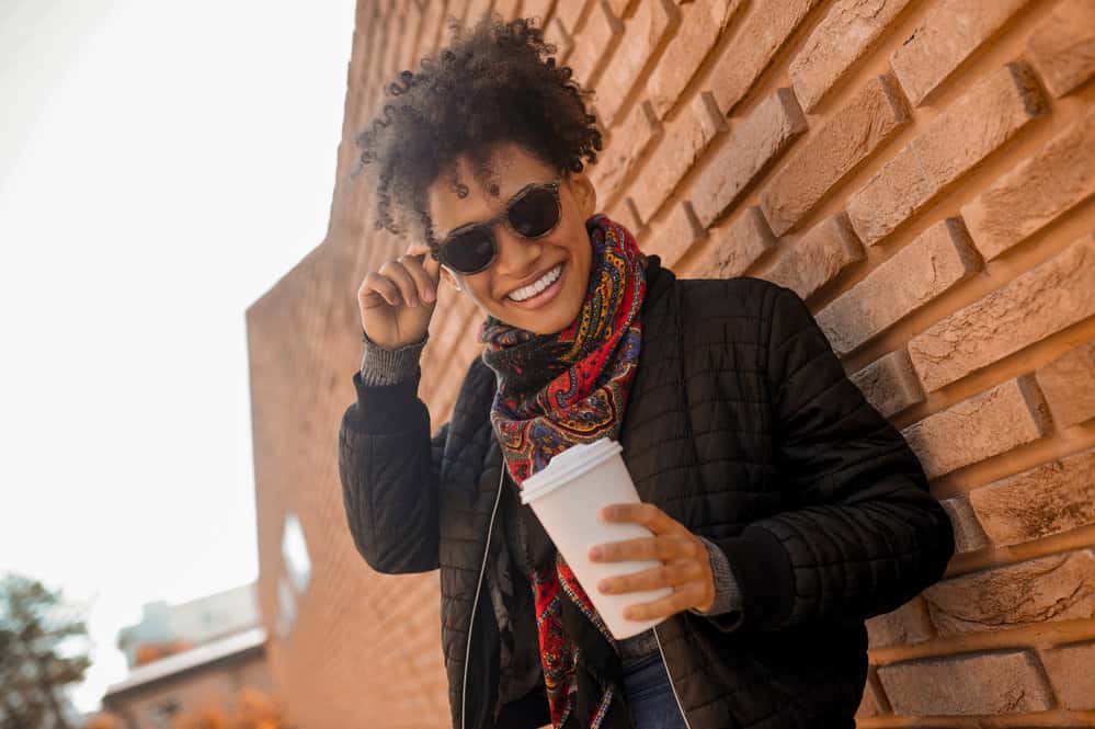 A cute girl with 3B tight corkscrews wearing dark sunglasses while drinking a cup of Starbucks coffee.