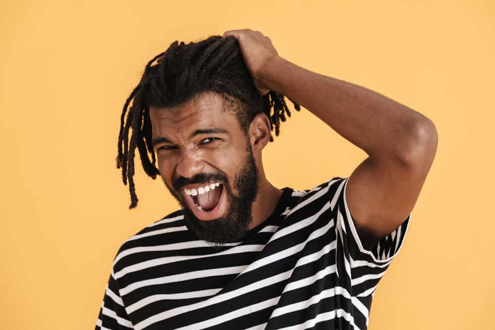 A black guy with healthy dreads is experiencing matted hair clumped together with hair flakes, like dandruff.