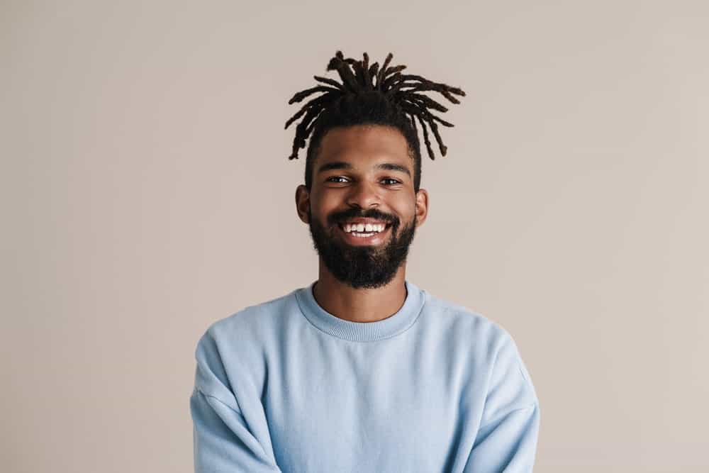 A black man with baby locs uses emollient oil and avocado oil to moisturize dry locs to keep his locs healthy.