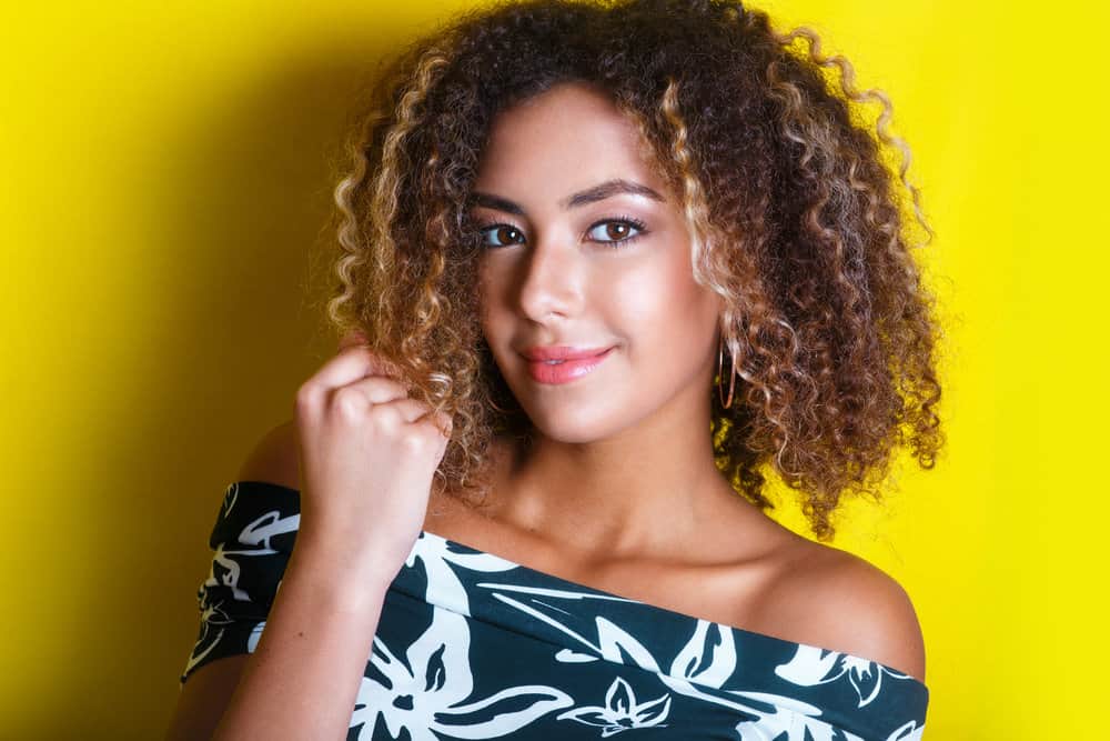 A cute black girl with natural curls created with either a lift or lightening process is evenly highlighted.