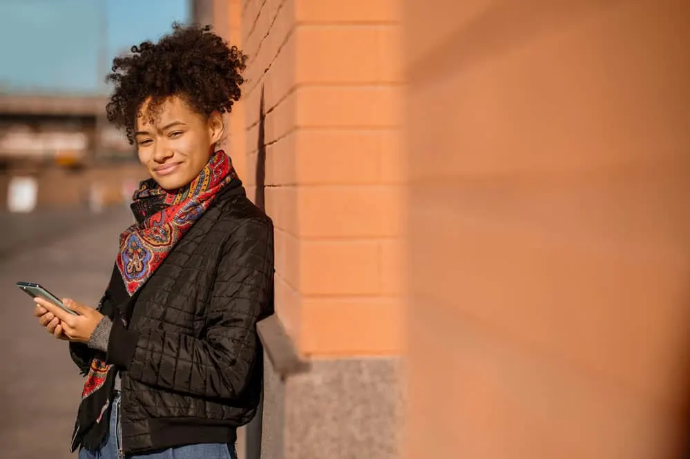 What Is 3C Hair? How To Take Care of It, Styles, and Products 9 A lady with type 3 curl definition is enjoying a fall day in the city while walking down a street with sidewalk chalk.
