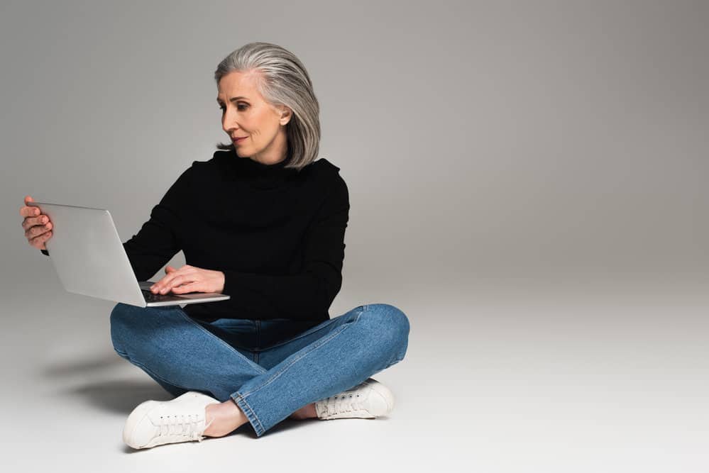 A 55-year-old middle age female wearing a causal outfit while researching what makes gray hair grow online.