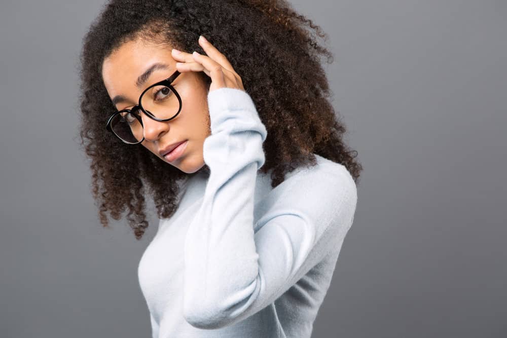 A young black girl with curly hair follicles colored with semi-permanent hair dye causing abnormal scalp irritation.