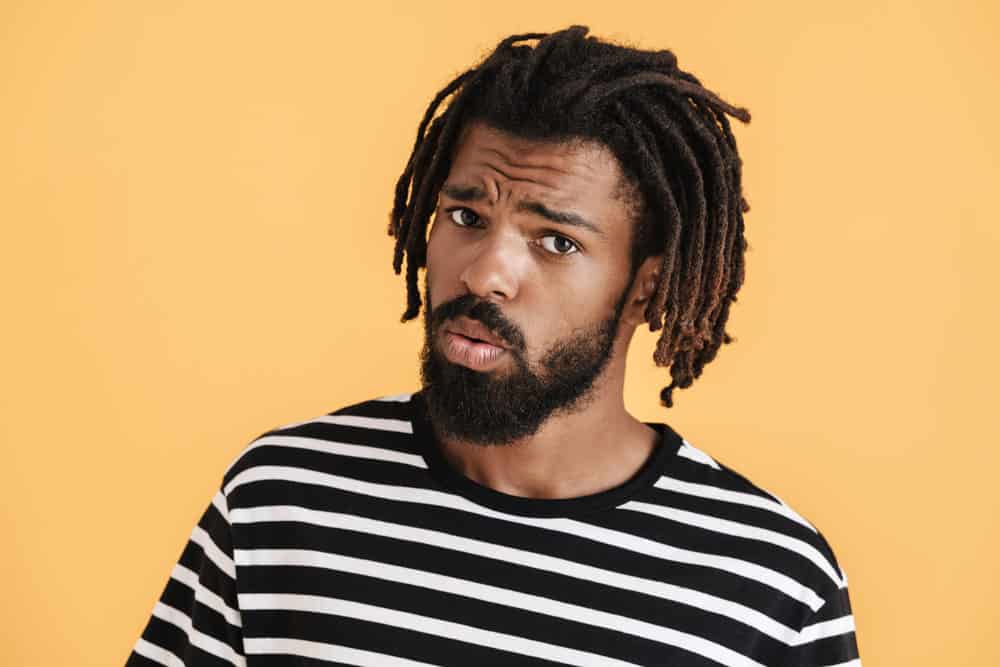 A confused black male with loose hairs is wondering how his approach to maintaining dreadlocks can be improved.
