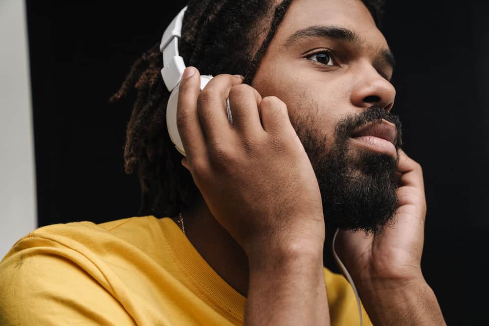 African guy with freeform dreads listening to the latest Cardi B album on his Beats headphones.