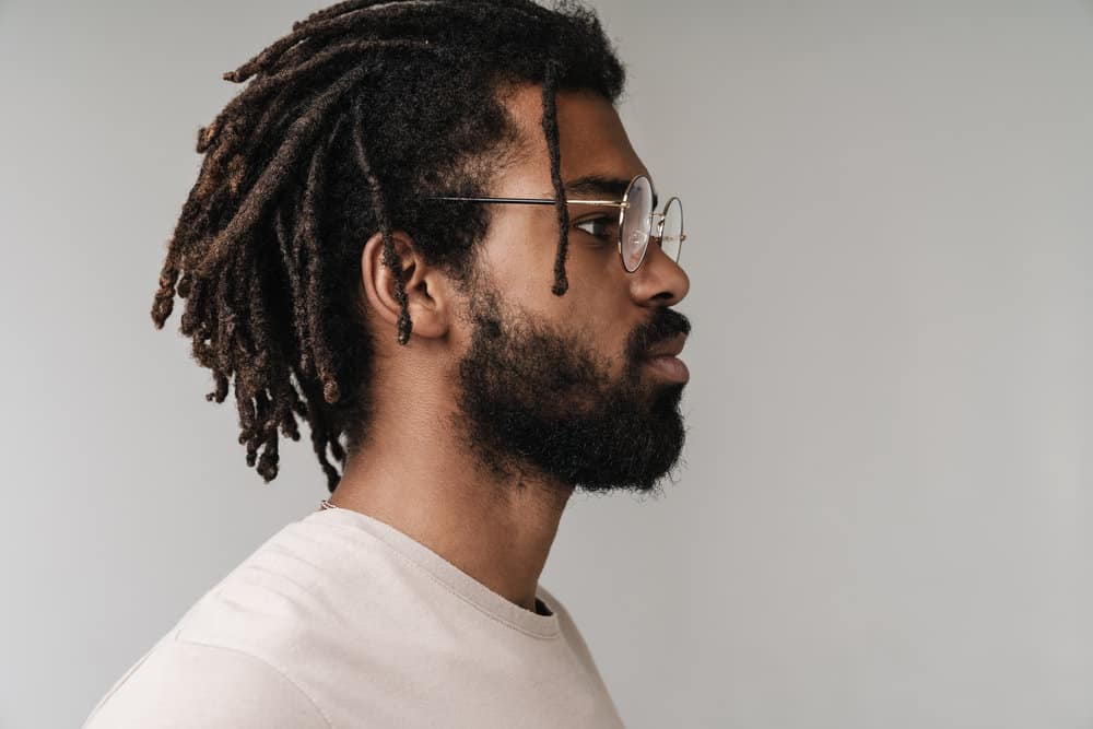 Side view of a serious black male that stores his hair oil with water in a convenient spray bottle to moisturize locs.