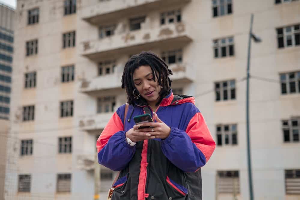 A young African American female with long locs researching 'how to sleep with dreads' on her mobile phone.