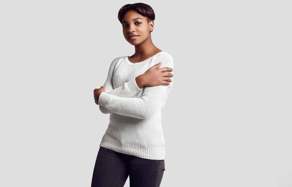 A woman wearing a white sweater with her arms crossed with beautiful dark red tones on her 3B hair strands.