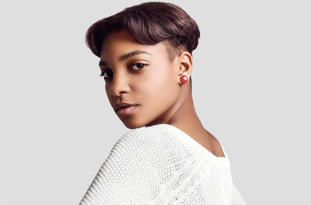 African American female with medium skin undertones wearing a dark auburn short hairdo with red pearl earrings.