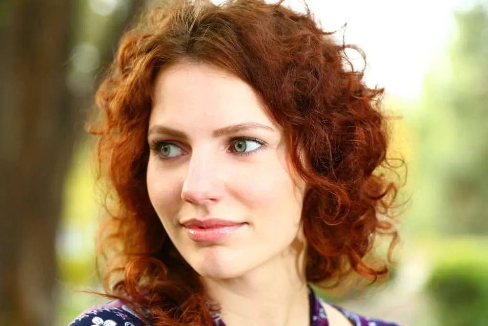 What Is 3A Hair? How To Take Care of It, Styles, and Products 2 A redheaded female with an S-shaped enhanced curl pattern in medium texture defined ringlets.