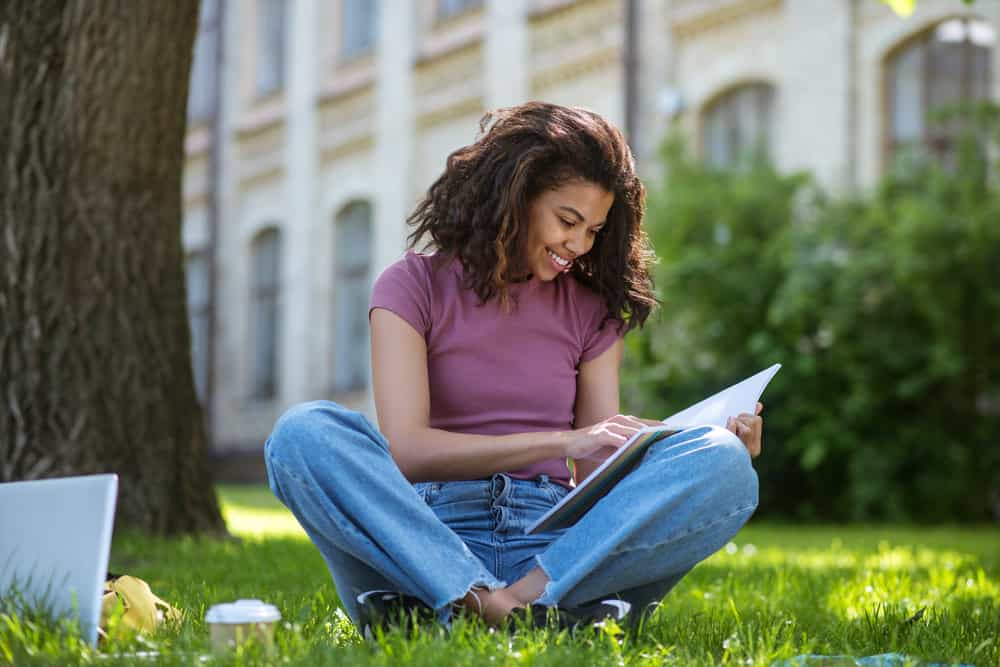 A female wearing a purple t-shirt writing a paper about essential amino acids and magnesium ions for beauty school.