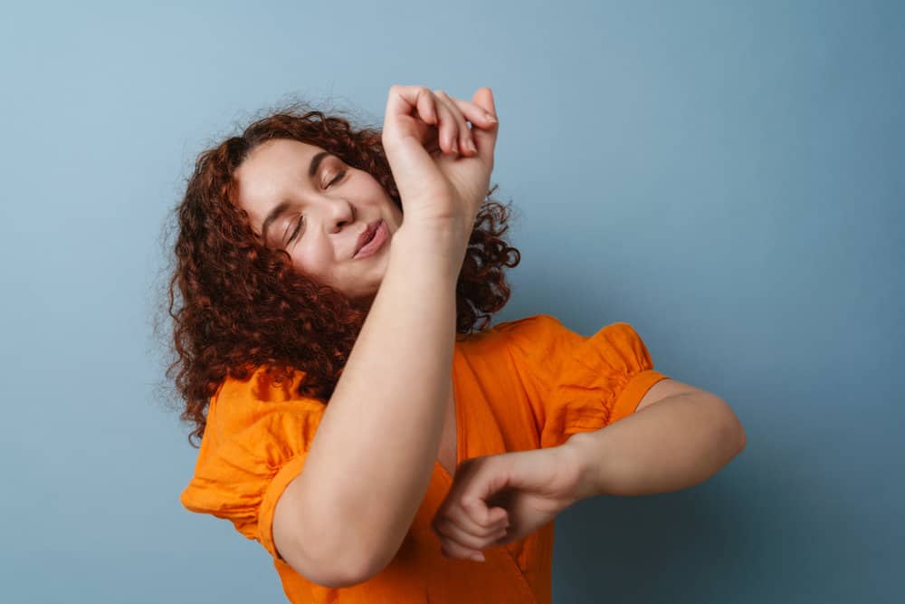 A joyful young female with red hair styled with canola oil and other natural ingredients is dancing indoors.