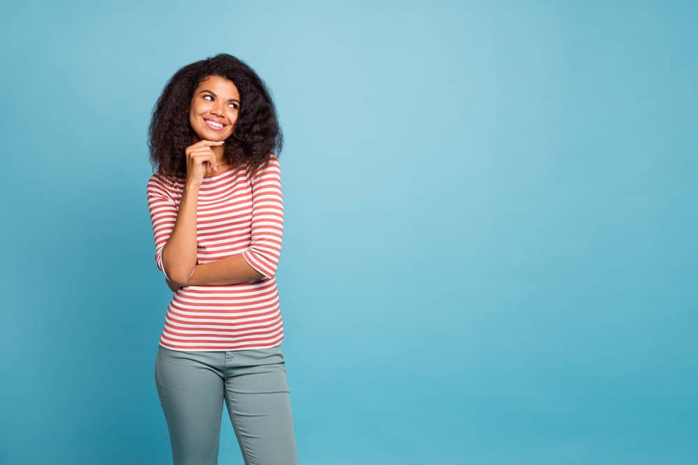 A young black lady, after getting her hair trimmed, is wearing a casual red and white shirt and blue jeans.