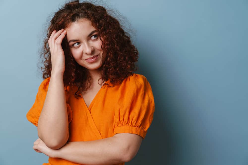 A young Caucasian female with curly hair follicles styled with olive oil after a hair mask is smiling and looking aside.