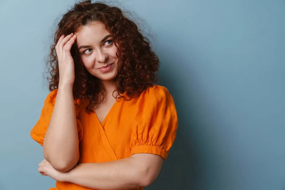 Get a Perm Out: How to Unperm Your Hair Naturally at Home 6 A young Caucasian female with curly hair follicles styled with olive oil after a hair mask is smiling and looking aside.