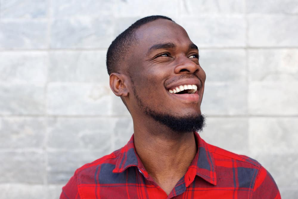 A young black wearing a low-skin fade haircut with a type 4 hair texture while sporting a plaid casual dress shirt.