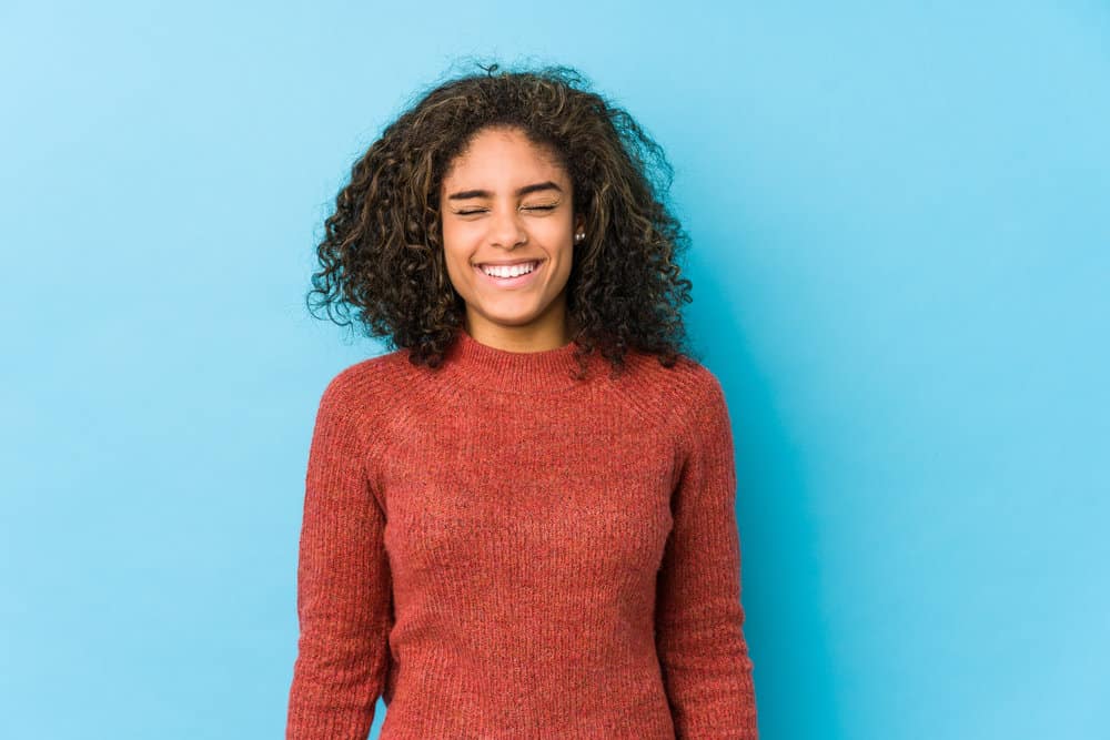 A cute black female is wearing a stylish sweater with curly hair styled with the right balance of shampoo and conditioner.