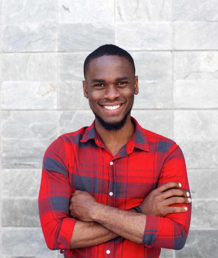 African male with his arms crossed while wearing a short hair fade with a bald side and one hair length on top.