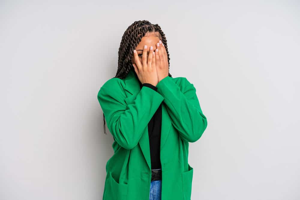 A black lady covering her face wearing tight twists in a style that looks like box braids more so than other hairstyles.