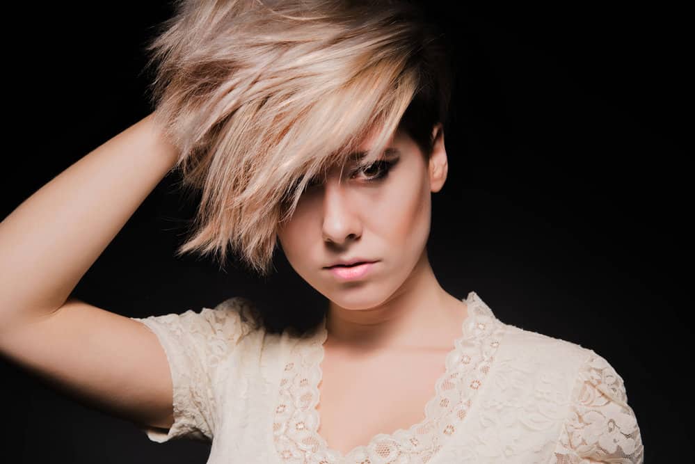 A Caucasian female is showing off the top layers of her shag cut where she has longer hair in the front than the back.