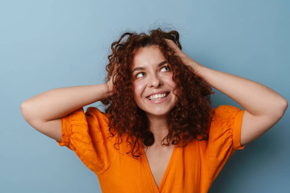 A young ginger female with damaged hair after getting her hair permed is experiencing hair breakage.