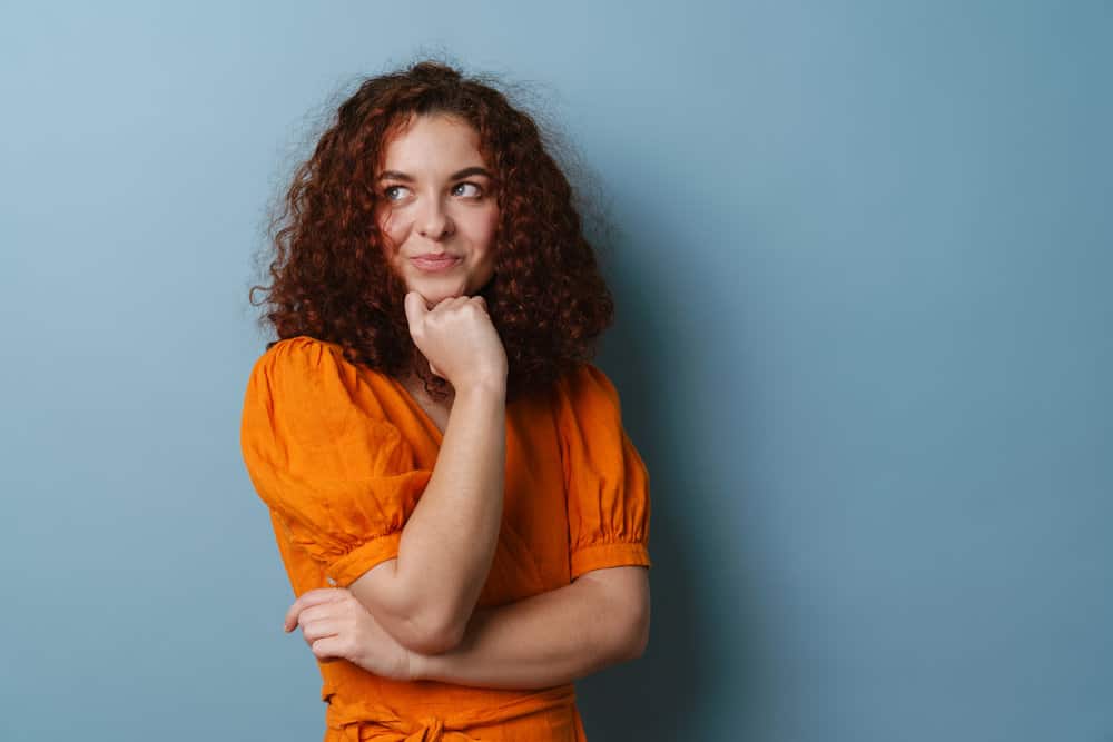 A beautiful lady with a subtle smile wearing an orange dress has her hair styled with a curling iron.