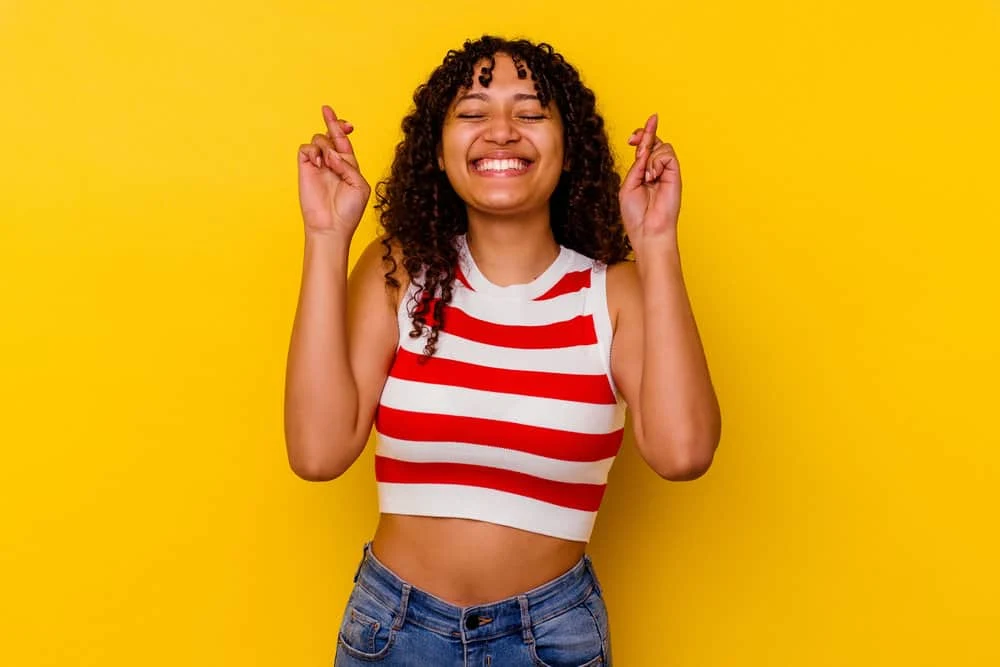 How to Stop Wave Nouveau Breakage: DIY Step-by-Step Guide 10 A young black female with kinky, curly hair strands is crossing her fingers, hoping that the Wave Nouveau perm works.