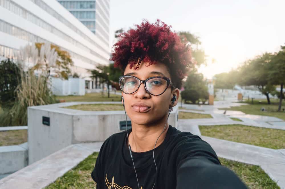 A woman with red and black curly bleached hair cleaned with an anti-dandruff shampoo and styled it with coconut oil.