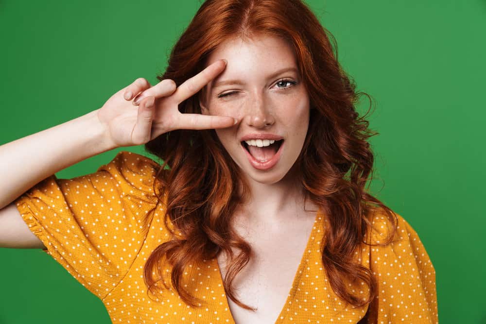 A joyful girl with dark hair wearing a beautiful orange dress while making a peace sign with her right hand.