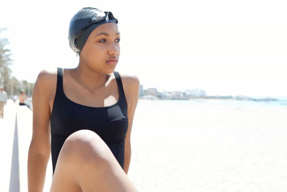 A beautiful African female wearing two swim caps made of silicone material for hair protection on a hot summer day.