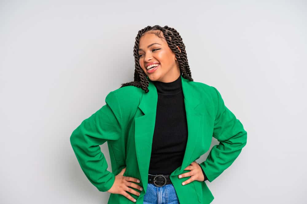 A woman wearing thicker, chunky twists has a great smile while wearing a green blazer and a black turtle neck.