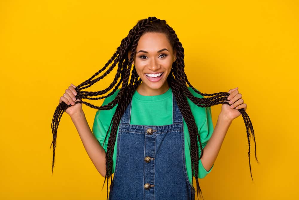 A cheerful African American wearing her hair braided with loose hair strands at the ends at the braids unravel.