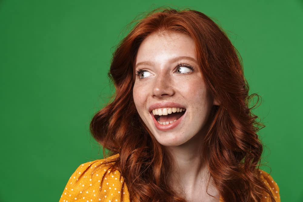 A female with freckles wearing an orange and white polka dot dress used hair bleach to dye her naturally black hair red.