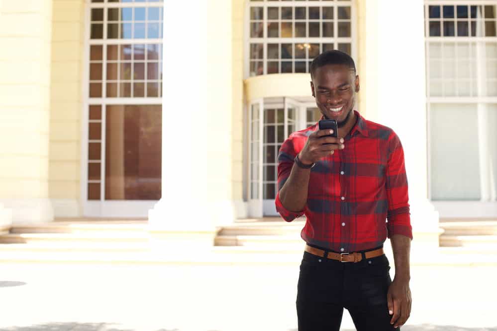 A handsome African male with naturally curly, wavy hair wearing a freshly cut mid-bald fade haircut with a line-up.