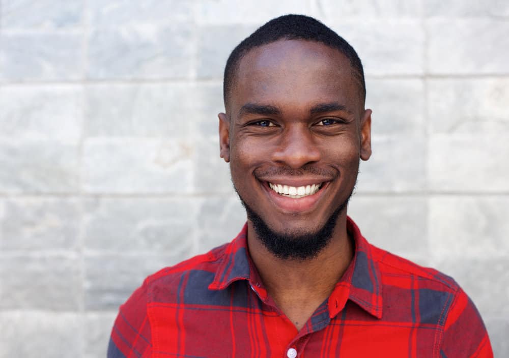 A happy male with a freshly cut mid-skin fade is showing a great smile and curly black beard with a low mustache.