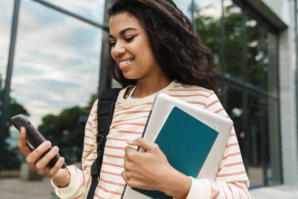 A smiling black woman girl using an iPhone has incredibly sleek locks following a flat ironing job and quick blow dry.