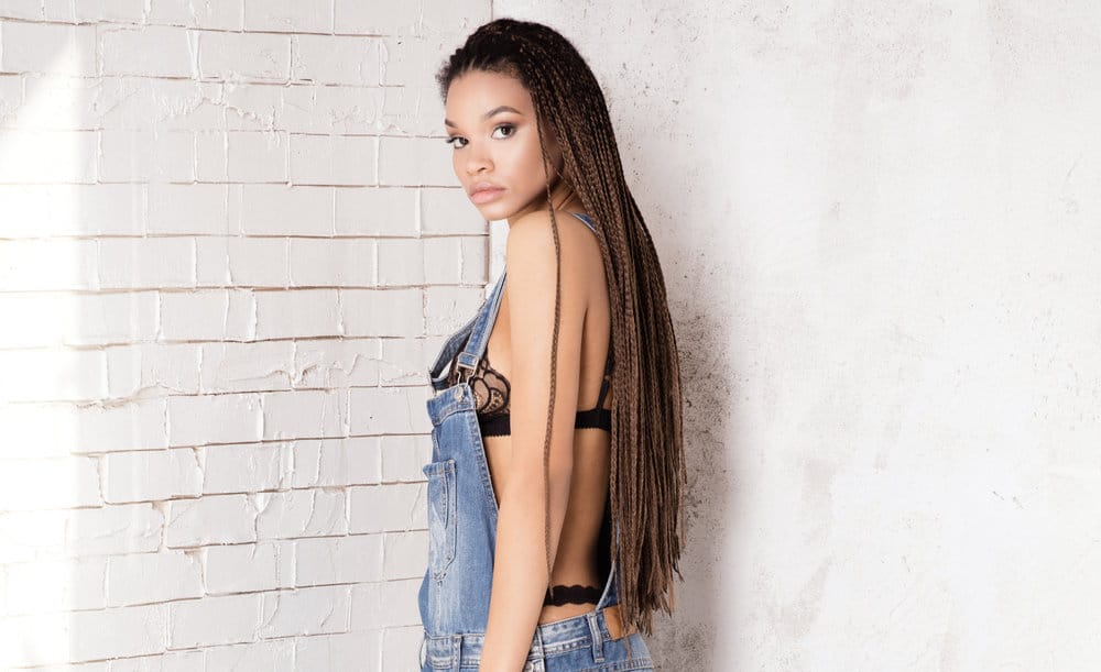 A black woman with long braids and straight hair at the tips as the extension hair appears to unravel.
