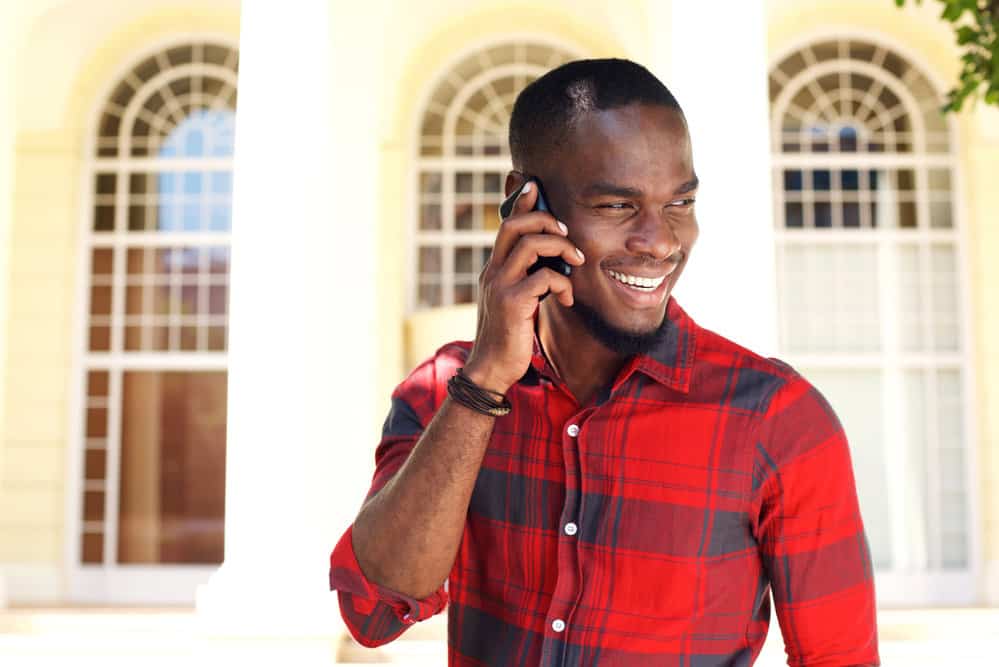 A black guy talking on a cell phone wearing a fade hair cut and a dark brown leather bracelet. 