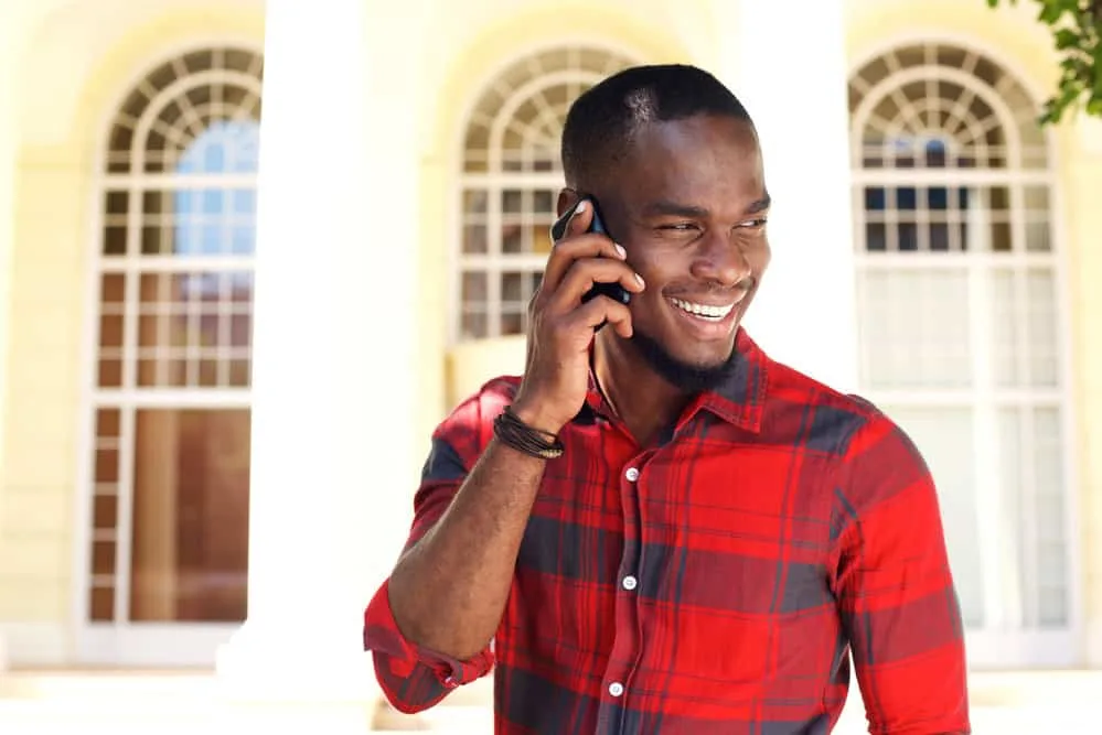 28 Different Types of Fades and Tapered Haircuts for Men 26 A black guy talking on a cell phone wearing a fade hair cut and a dark brown leather bracelet.