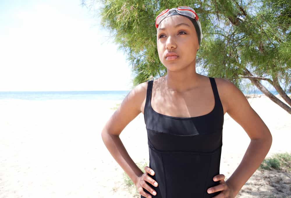 African American with brittle hair preparing to go for a swim while standing on the beach with regular swimmers.