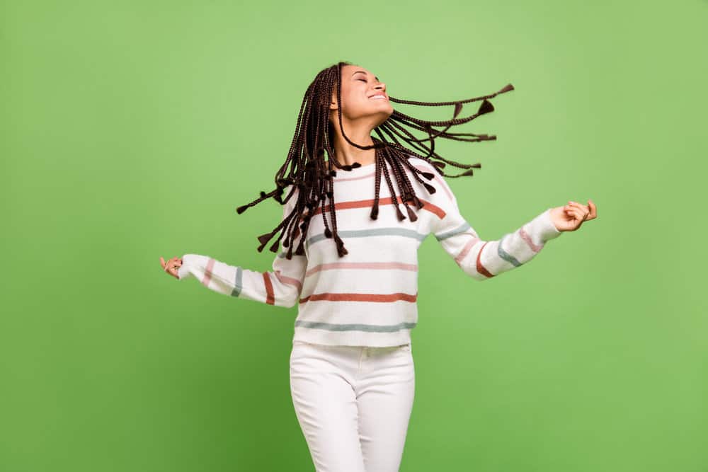 A young female wearing a braided synthetic wig is enjoying music while dancing.