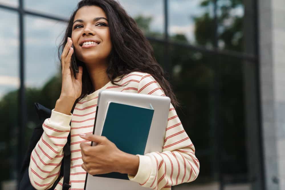 A light-skinned black female talking on the phone while wearing beach waves elongated with a straightening technique.