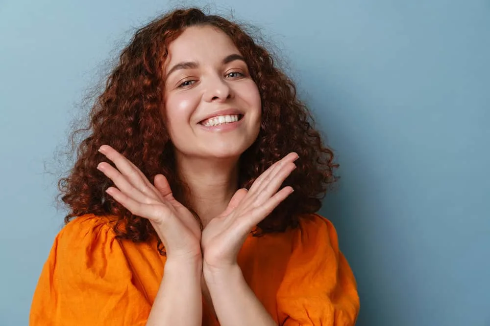 Get a Perm Out: How to Unperm Your Hair Naturally at Home 8 A lady with naturally curly red hair styled with natural remedies and perm rods is wearing an orange dress.