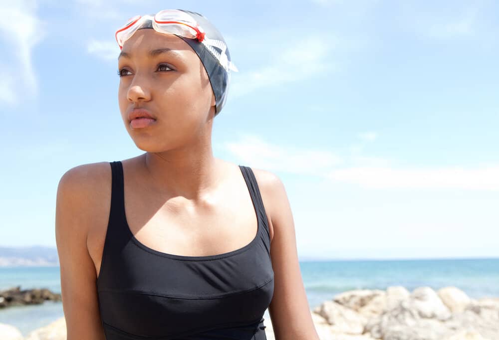 A sporty African American young swimmer that keeps her hair strands tucked under silicone swim caps.