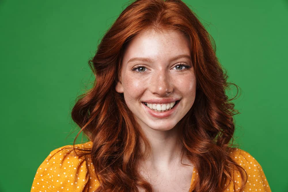 A girl with naturally dark brown hair that's starting to develop red tones with a reddish tint on her color-treated hair strands.