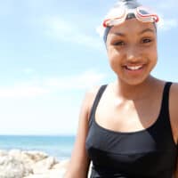 A young black girl with long hair wearing a silicone cap to keep her hair healthy and avoid pool chemicals.