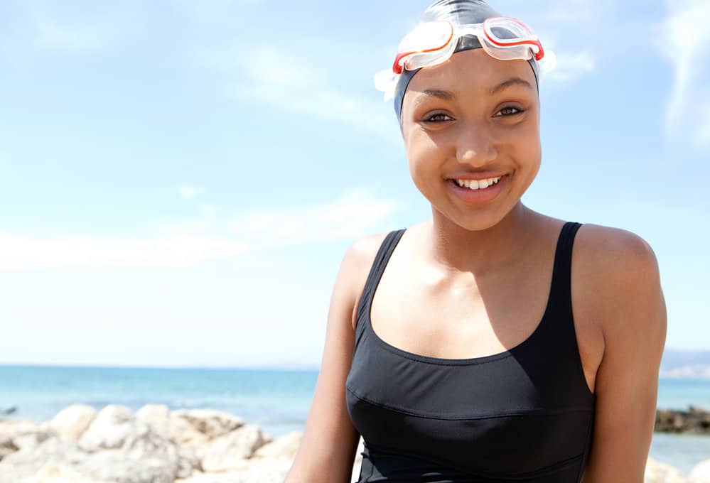 A young black girl with long hair wearing a silicone cap to keep her hair healthy and avoid pool chemicals.