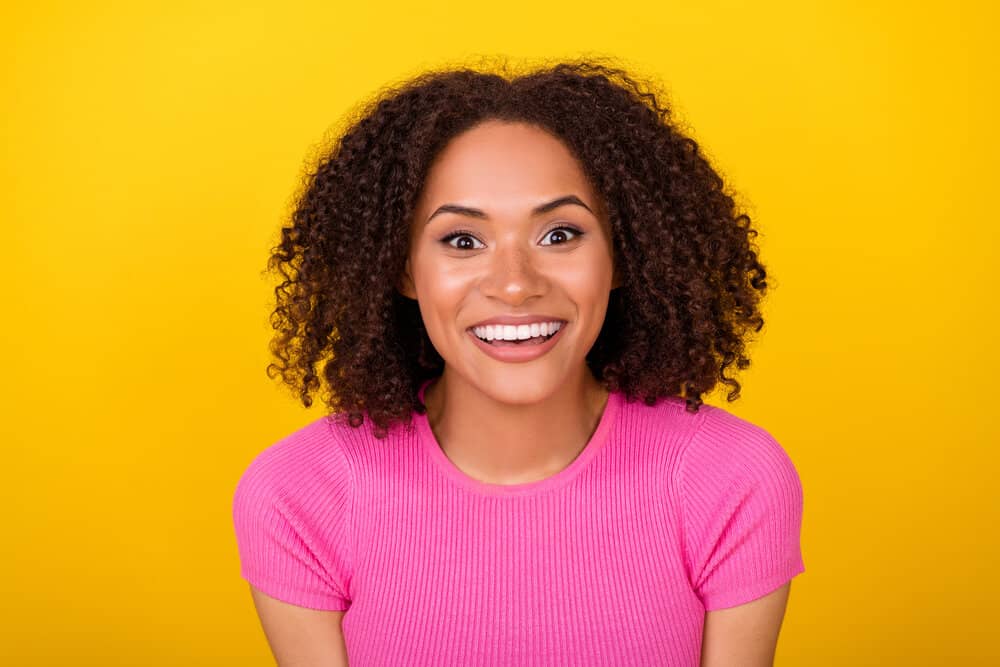 A cheerful young female wearing her curls in a shoulder-length wash-n-go style after letting her hair dry naturally.