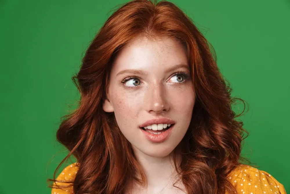 Why Is My Hair Turning Red Naturally? Becoming a Redhead? 2 A young female with light brown and red strands wash her hair with purple shampoo and styled it with basic hair oil.