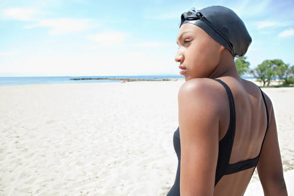 Side portrait of a light-skinned black girl with thick hair wearing a lycra swim cap like most competitive swimmers.